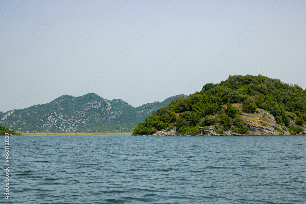 Landscape with lake and green mountains against the background of a clear sky. Panoramic beautiful view on largest lake. Wonderful summer day.