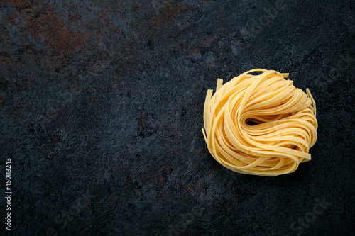 Fresh raw tagliolini pasta rolled with a nest on a stone background. Type of Italian pasta, top view and copy space