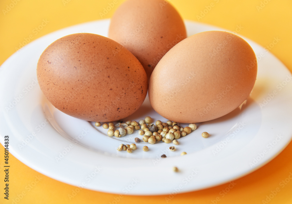 Chicken eggs placed on white plate with some white pepper on color background Chicken eggs placed on white plate with some white pepper on color background