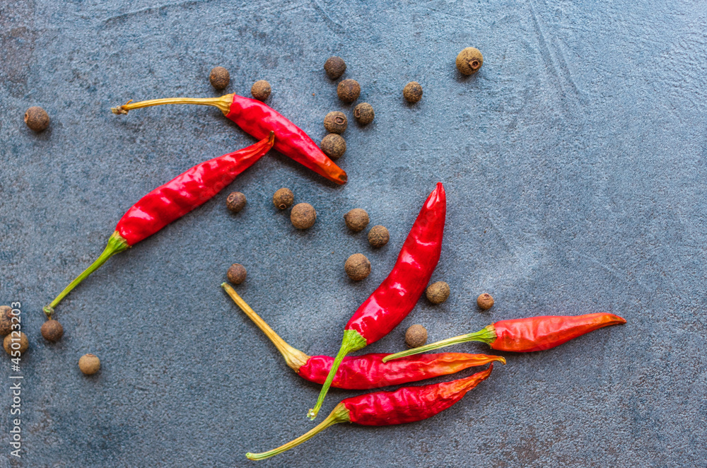 Spices of black pepper and red hot pepper lie on a cutting board made of dark stone Spices of black pepper and red hot pepper lie on a cutting board made of dark stone