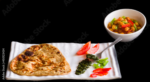 Homemade Indian flat bread known as Parantha,served with Chickpea gravy also known as Chole or Chana. Garnished with Coriander and Mint Dip, commonly called Chutney. Dark background. Front view.