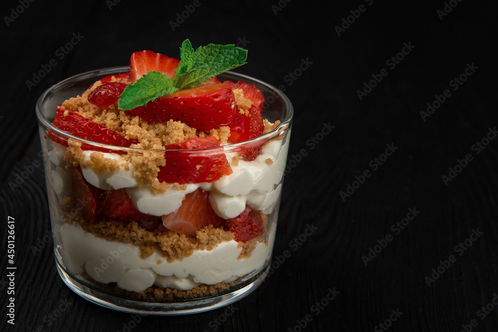 Strawberry with cookie and cream dessert decorated with mint leaf on black wooden background, with copyspace Strawberry with cookie and cream dessert decorated with mint leaf on black wooden background, with copyspace