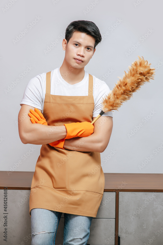 Young man pose with feather duster cleaning furniture at home Young man pose with feather duster cleaning furniture at home