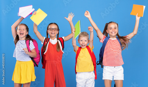 Funny kids with backpacks behind happily jumping raising their hands up with exercise books