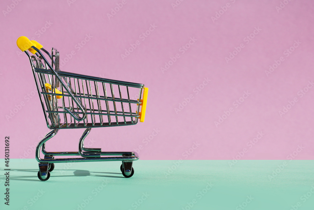 Small supermarket grocery push cart for shopping toy with wheels on violet-green background. the concept of consumption, in-store purchases, sales