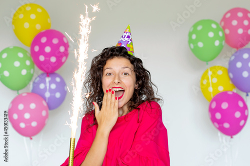 Happy Birthday. Sexy brunette girl posing with balloons, fireworks, colorful balloons and holiday cake on a white background