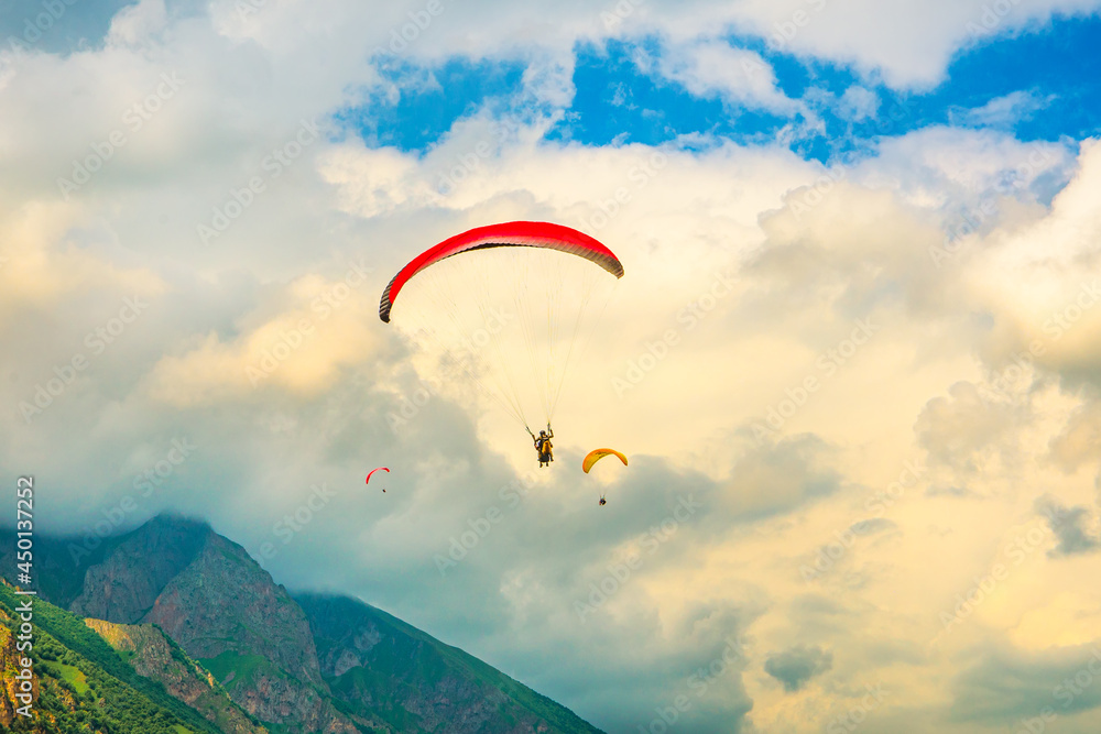A paraglider flies high in the mountains against the background of an epic sky A paraglider flies high in the mountains against the background of an epic sky
