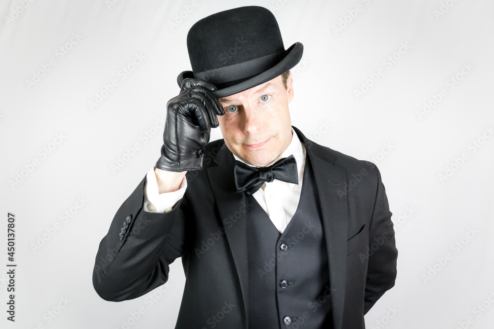 Portrait of British Gentleman in Dark Suit and Leather Gloves Politely Doffing Bowler Hat. Concept of Butler and Professional Hospitality. Vintage Style and Fashion. Portrait of British Gentleman in Dark Suit and Leather Gloves Politely Doffing Bowler Hat. Concept of Butler and Professional Hospitality. Vintage Style and Fashion.