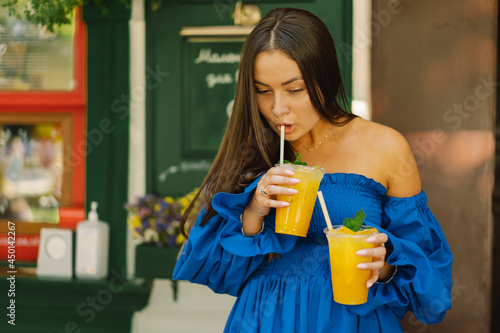 Portrait happy young woman wearing blue dress and drinking summer cocktail lemonade