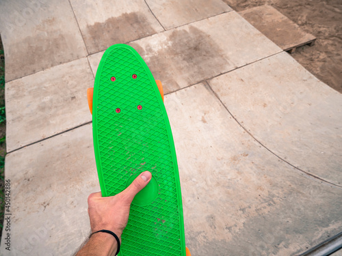 Male hand holding a green penny board in a skatepark. photo