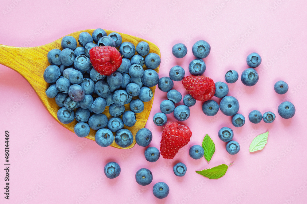 Bilberries and raspberries on wooden spoon. Pink paper background, free space for text Bilberries and raspberries on wooden spoon. Pink paper background, free space for text