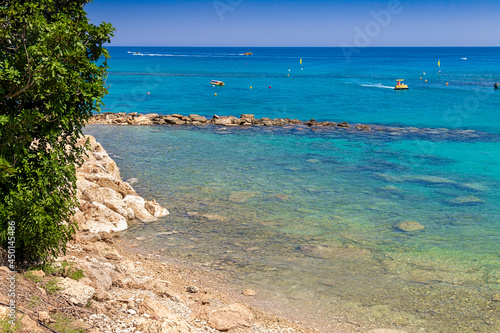 Rocky part of the urban beach of Fig Tree Bay in Protaras  Cyprus. Catamarans  jet skis and boats are visible in the distance. Azure Mediterranean Sea.