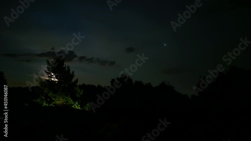 time-lapse. The moon slowly rises above the horizon, from behind the tree to the sky tightly covered with clouds. photo