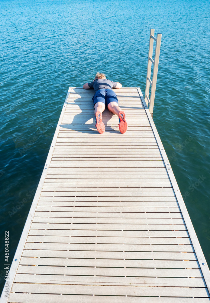 Boy lying on wooden pier over a lake watch fish in  blue water below