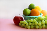 fresh fruit in the basket apple, lime, avocado, lemon, orange, grapes on a light pink background