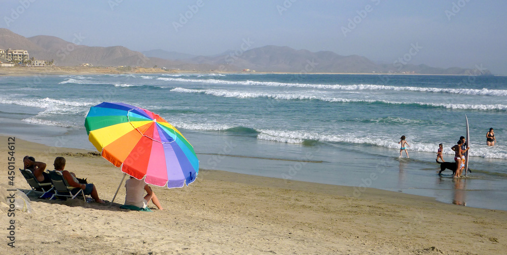 Sombrilla y gente en playa con mar y tabla de surf