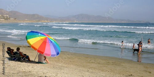 Sombrilla y gente en playa con mar y tabla de surf photo