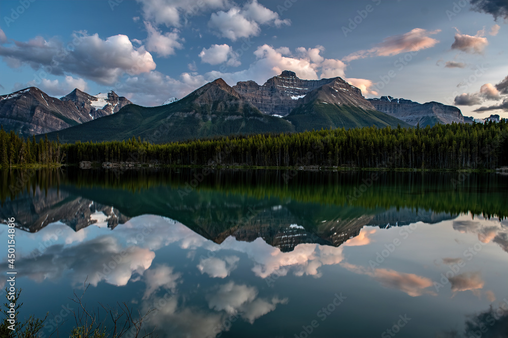 MOUNTAINS AND CLOUDS REFLECT OFF THE SURFACE OF HERBERT LAKE AT DUSK - BANFF NP