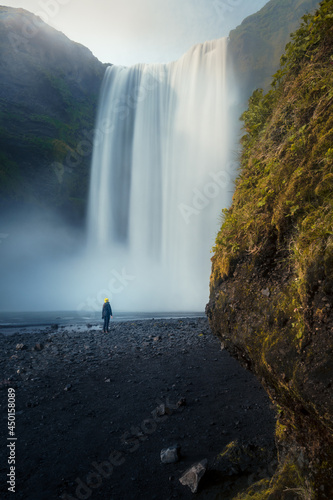 Moody view of female person standing in front of gigantic Skógafoss waterfall