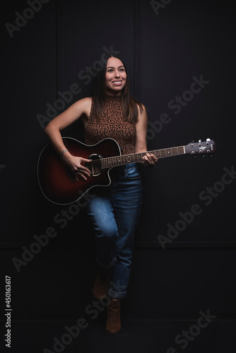 Vertical of a beautiful young latina with a guitar in her hands and a black background.