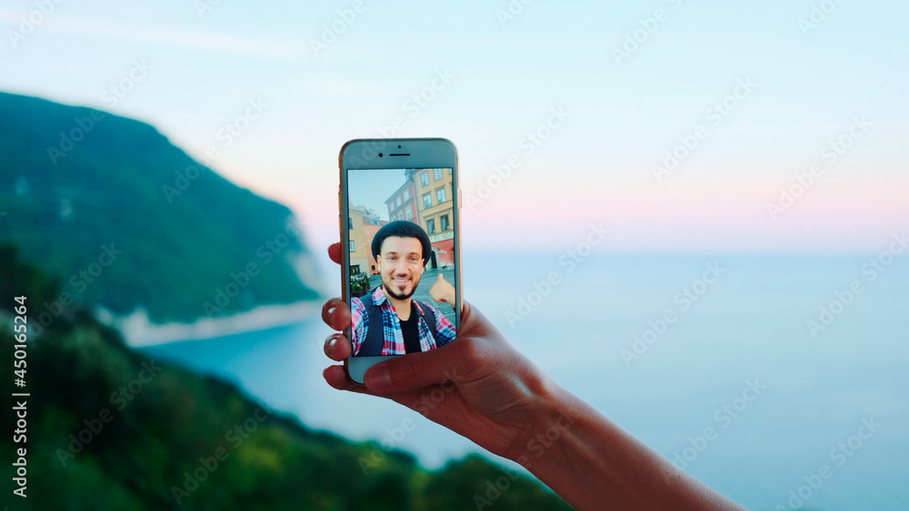 Hand holding smartphone during video call with man in front of the sea. Beautiful landscape in the background.