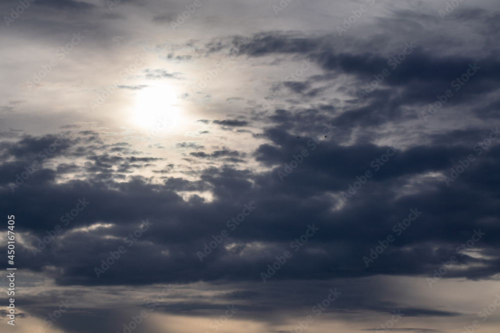 Dark stormy high clouds framing sky with sun shining through clouds, cloudscape background. Skyscape natural scenery