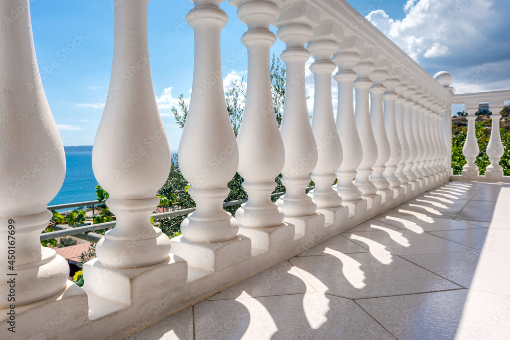 Traditional white balusters close-up. Greek architecture elements of terrace. View through balcony on clear blue Aegean sea coast. Summer country house near Athens, Greece