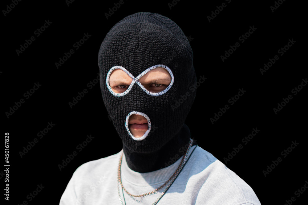 Closeup headshot of criminal wearing black balaclava and hoodie looking at camera, copy space, isolated over black background. crime and violence, drugs, fashion, rap, rapper new school. Closeup headshot of criminal wearing black balaclava and hoodie looking at camera, copy space, isolated over black background. crime and violence, drugs, fashion, rap, rapper new school.