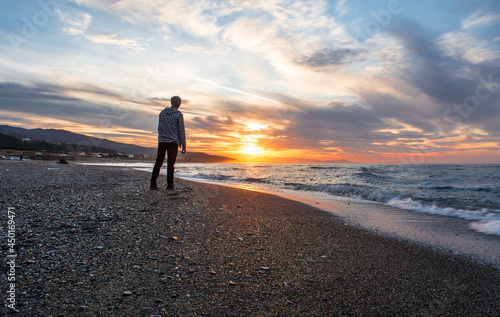Young man in sandy beach watching and meditating on beautiful sun in sandy beach watching and meditating on beautiful sunset, landscape of sunset, clouds and blue sky in the Mediterranean Sea, Algeria