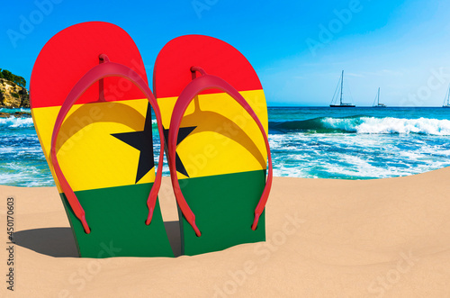 Flip flops with Ghanaian flag on the beach. Ghana resorts, vacation, tours, travel packages concept. 3D rendering
