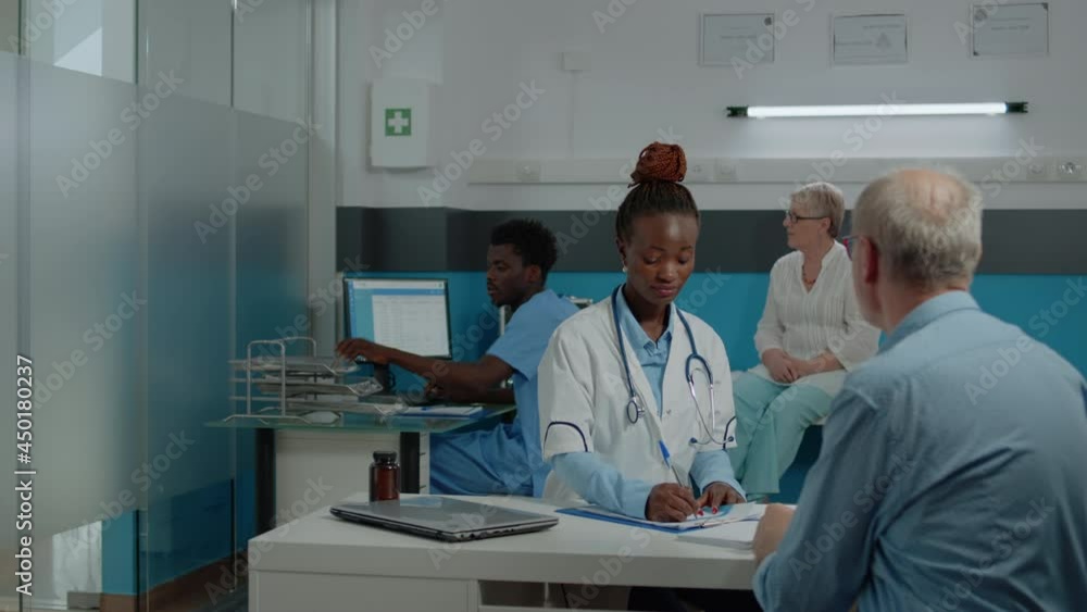 Young medical assistant giving x ray to doctor sitting at desk with elder patient for scan results analysis in office. Medic holding radiography while old man looking at healthcare diagnosis Young medical assistant giving x ray to doctor sitting at desk with elder patient for scan results analysis in office. Medic holding radiography while old man looking at healthcare diagnosis