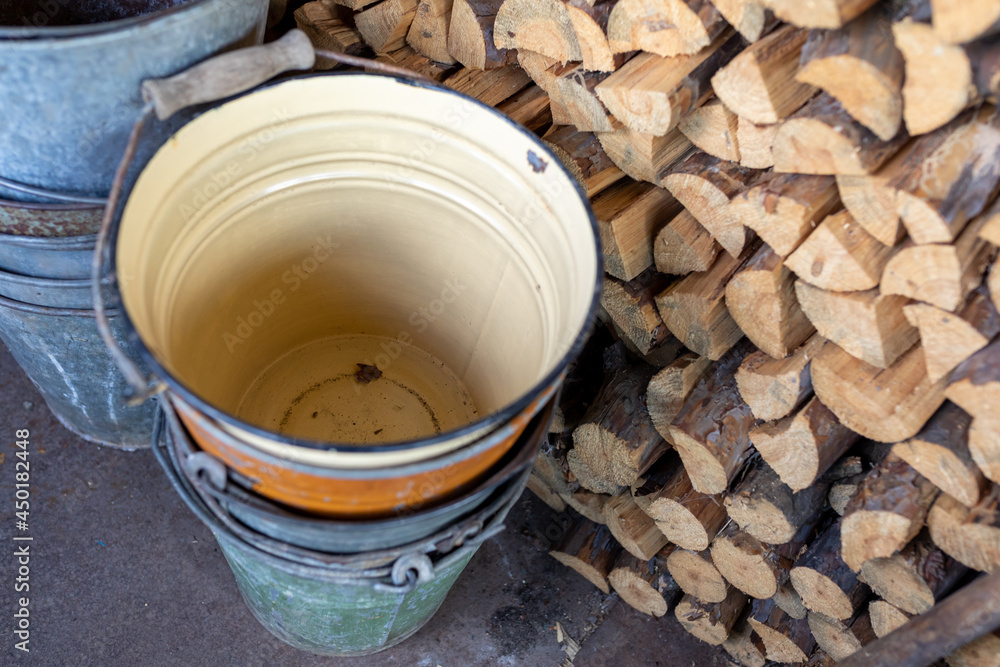 old metal buckets stand in shed near stack of chopped firewood old metal buckets stand in shed near stack of chopped firewood