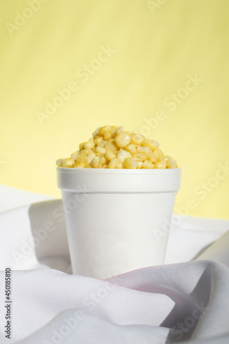 Elote en vaso de unicel con fondo amarillo sobre tela blanca photo