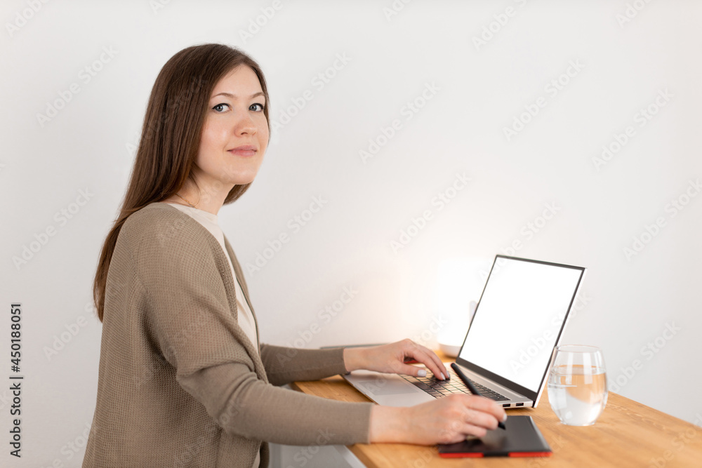 Attractive young caucasian female working at the laptop and digital tablet. Graphic designer working from home office. Empty blank white screen, copy space. Wooden workspace. Freelance concept. Attractive young caucasian female working at the laptop and digital tablet. Graphic designer working from home office. Empty blank white screen, copy space. Wooden workspace. Freelance concept.