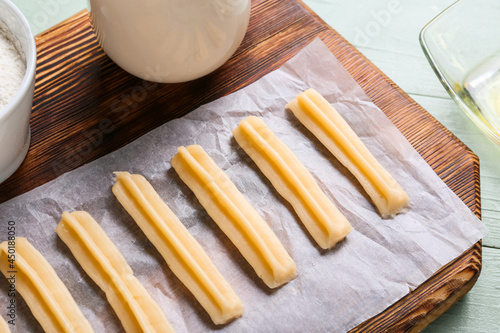 Board with uncooked churros on color wooden background, closeup