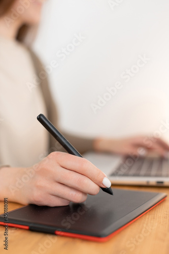 Graphic designer work with digital tablet and laptop. Wooden workspace. Woman freelancer work from home office. Selective focus on hand with pencil, blurred background. Close up photo.