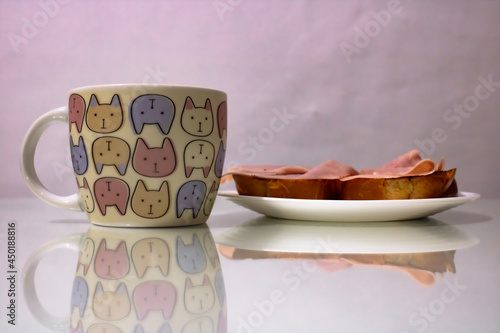 white plate with two slices of bread with ham and a mug of kittens photo