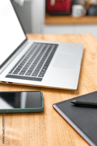 Grey laptop, black digital graphic tablet and smartphone on wooden desk. Gadgets for working from home office or surfing in web. Communication concept. Selective focus on pencil, blurred background.