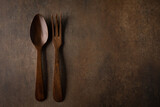 A rustic brown textured background with dark wood fork and spoon serving utensils