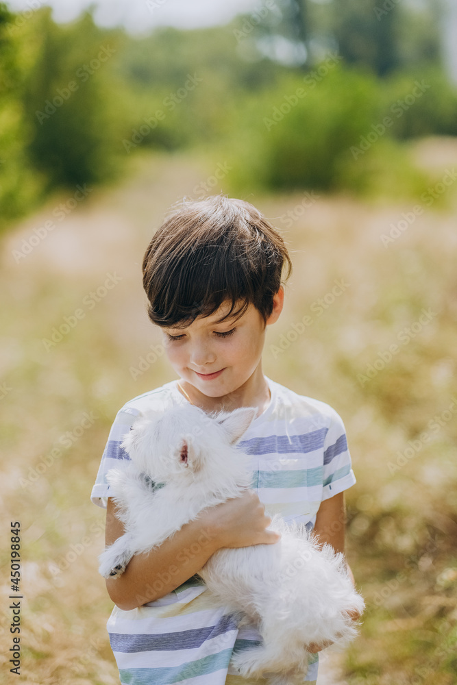 Friendship of a child with a dog. Happy boy holding a West Highland White Terrier puppy in his arms. Friendship of a child with a dog. Happy boy holding a West Highland White Terrier puppy in his arms.