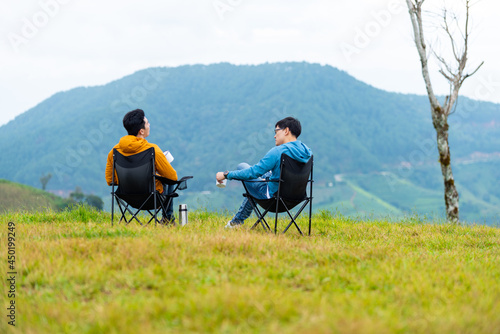 Asian man friends sitting on outdoor chair on the mountain drinking hot coffee together. Male friendship enjoy outdoor activity active lifestyle hiking and camping together on summer vacation. photo