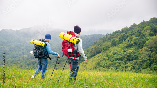  Two handsome Asian people man friends with backpack hiking together on mountain trail. Healthy male friendship enjoy outdoor activity and active lifestyle climbing and camping in summer vacation.