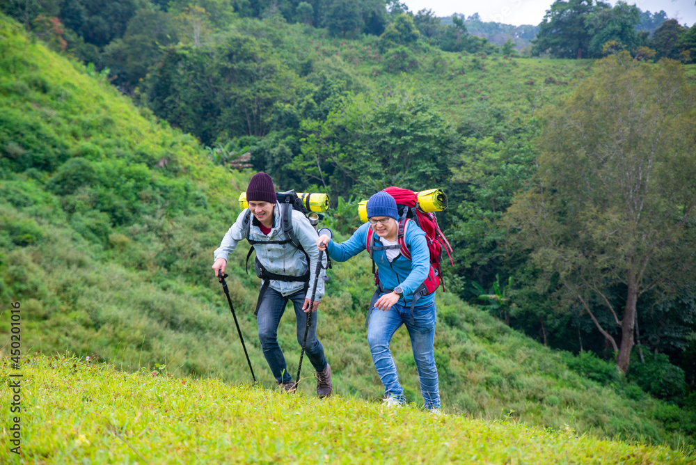  Two handsome Asian people man friends with backpack hiking together on mountain trail. Healthy male friendship enjoy outdoor activity and active lifestyle climbing and camping in summer vacation.
