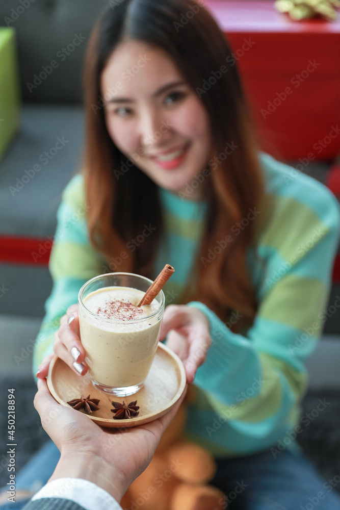 Glass of tasty eggnog drink with chocolate stick and nutmeg, as traditional beverage for happy Christmas holiday festival, served to pretty Asian woman on green sweatshirt with smiling face Glass of tasty eggnog drink with chocolate stick and nutmeg, as traditional beverage for happy Christmas holiday festival, served to pretty Asian woman on green sweatshirt with smiling face
