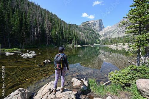 Young woman enjoys view of Dream Lake from Emerald Lake Trail in Rocky Mountain National Park, Colorado on calm summer morning.
