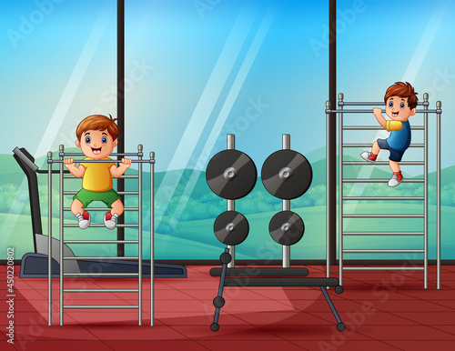 Cheerful little boys pulling himself up on a sport horizontal bar in a gym