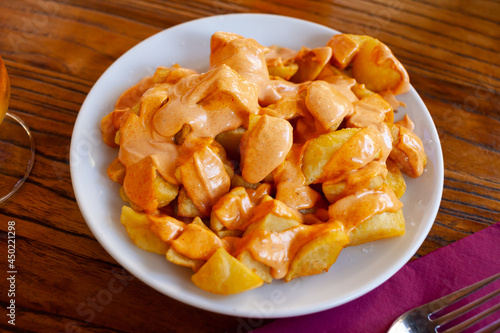 Traditional Spanish fried potatoes Patatas bravas served with cheese sauce and spicy sauce with paprika and chili © JackF