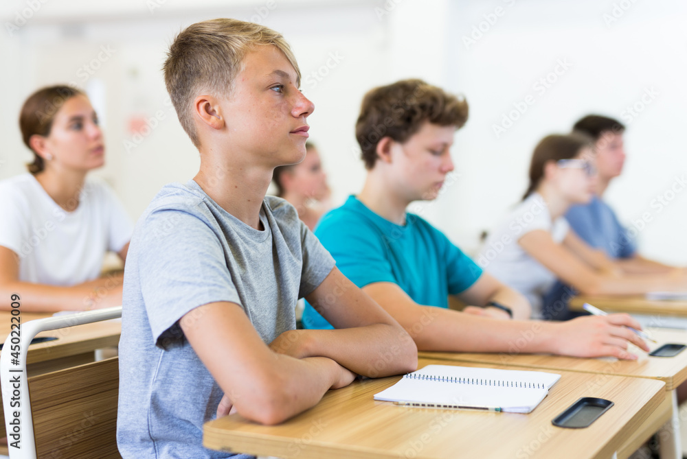 Teenager students sitting at desks and listening. Boy sitting in foreground.