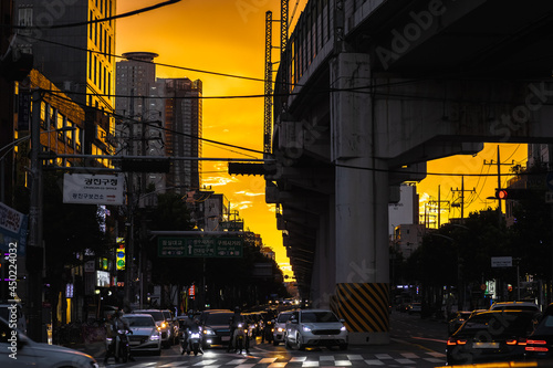 복잡한 서울 도심의 교통 체증, 건물과 지하철 지상 구간의 고가 철로 교량 사이 오렌지색 노을 풍경