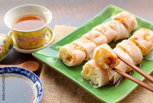 Steamed rice noodles wrapped with Chinese fried dough- Cantonese dim sum called Zhaliang or Cheong fun served with sweet soy sauce at close up view photo